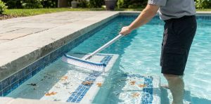 A submerged pool vacuum head moving across the bottom of a clear pool, actively suctioning settled dirt and leaves from the plaster floor.