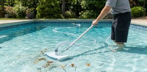 A submerged pool vacuum head moving across the bottom of a clear pool, actively suctioning settled dirt and leaves from the plaster floor.